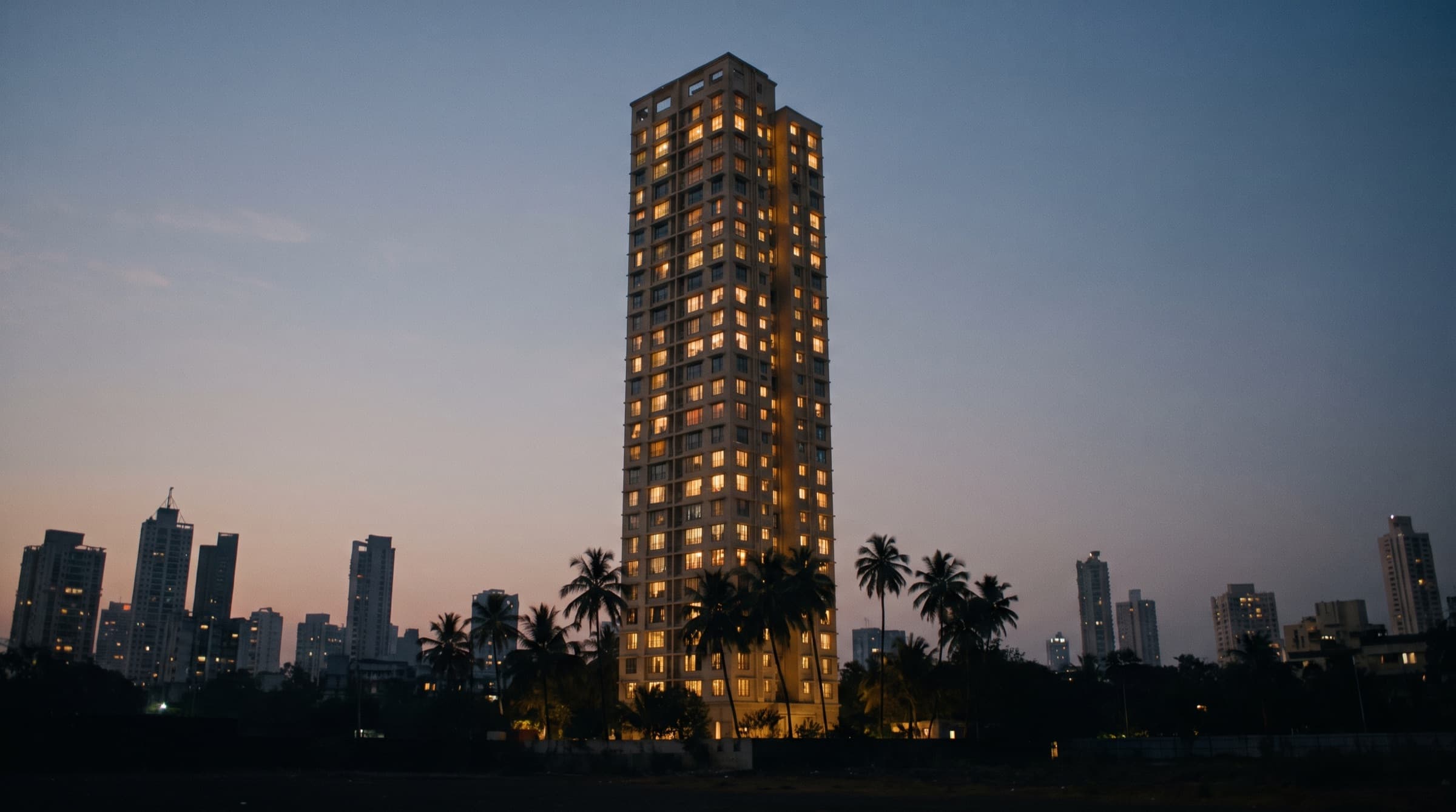 A high-rise residential tower lit up at dusk against a city skyline (representative image)